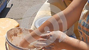 The sculptor potter`s work hands on the street makes jug out of clay closeup. Twisted potter`s wheel.
