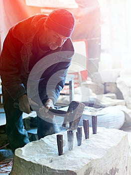 The sculptor of the stone-maker strikes with a heavy hammer on w