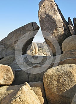 Sculptural granite boulders against a blue sky, forming a triangular window to the desert landscape beyond