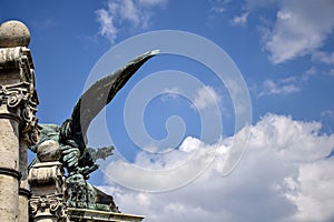 The sculptural image of a formidable eagle on an ancient colonade against blue sky with clouds. Turul Eagle Statue at main gate of