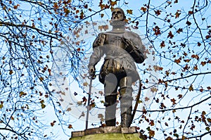 Sculpture against the clear blue sky surrounded by autumn trees with dark leaves withered