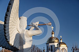 Sculpture of angel with a wind instrument against the background of the Orthodox Church