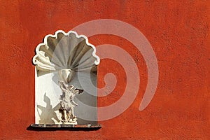 Sculpture of the Archangel Michael against the background of the old red wall. Architectural vintage background. Mexico.