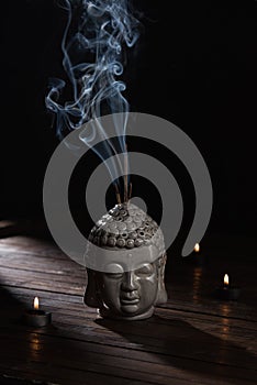 Sculpture of buddha head with burning incense sticks and candles