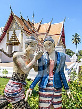 Sculpture of couple of Burmese lovers in a whispering manner with famous Wat Phumin buddhist temple in the background in Nan city