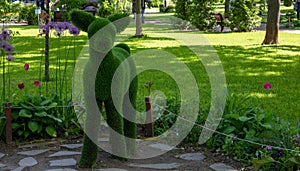 Sculpture of a fawn in a green park against a background of trees and flowers on a bright sunny day