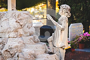 Sculpture of little angel girl at old cemetery. Closeup of stoned angel at cemetery. Graveyard old weathered stone baby statue on