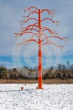 sculpture of many basketball hoops on orange pole under blue sky in Winter snow