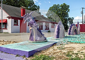 Sculpture of a purple dragon snake undulating in and out of a sidewalk beside rocky ground in Dallas, Texas.