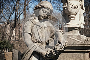 A sculpture of sad woman in grief. Virgin Mary stone statue near the funeral urn suffering, death concept