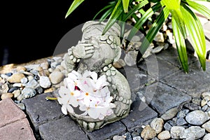 Sculpture thai girl doll with plumeria flower in the pebble garden