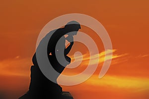 Sculpture thinking man in sunset silhouette. Concept photo