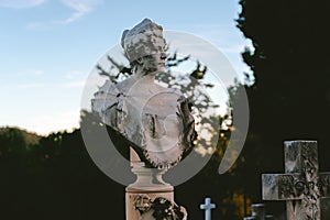 Sculpture of a woman at old cemetery. Portrait of stone figure and cross monument at cemetery. Old stone Graveyard statue on funer