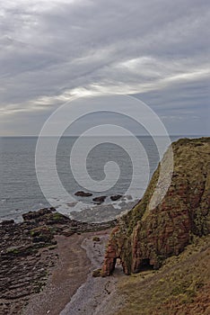 The Sea Arch below Maw Skelly Headland and Sea Cliffs on and above the narrow Shingle Beach and rocky outcrops.