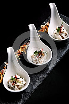 Sea bass ceviche mini portions served in beautiful Chinese spoons on a black plateau. Food concept for catering.