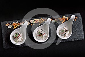 Sea bass ceviche mini portions served in beautiful Chinese spoons on a black plateau. Food concept for catering.