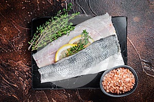 Sea Bass fillets, Raw Seabass fish with thyme, pink salt and lemon on marble board. Dark background. Top view