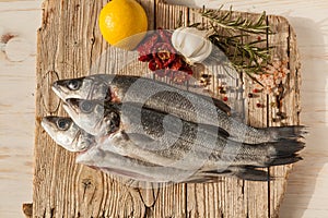 Sea bass fish with garlic, rosemary, tomatos and lemon on a wood table from above