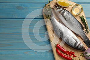 Sea bass fish and ingredients on light blue wooden table, top view. Space for text