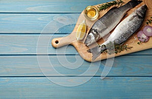 Sea bass fish and ingredients on light blue wooden table, top view. Space for text