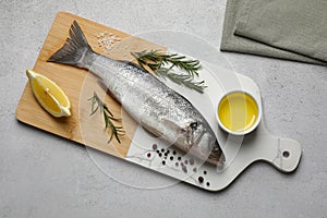 Sea bass fish and ingredients on light grey table, top view