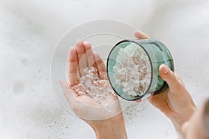 Sea bath salt in woman hands against the background of foam bath.