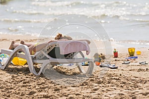 On sea beach near the water with a beach chair sunbathing girl, spanking and childrens sand toys