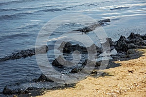 The sea and the beach are polluted with oil. A crude oil spill on the sand of a city beach. Beach oil spill impact, pollution,