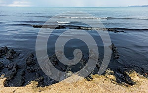 The sea and the beach are polluted with oil. A crude oil spill on the sand of a city beach. Beach oil spill impact, pollution,