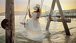 Sea beach with a rope swing, where a woman in a flowing dress savors the sway during sunset. Spirit of tourism, the