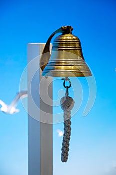 A sea bell or a rynda hanging on a wooden pole against a background of blue sky and seagulls.