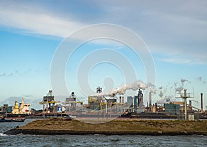 Sea with boats ailing and a big factory in the distance under a blue sky