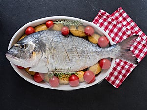 Sea bream, tomatos, potatos and rosemary on a serving dish on slate background. ready to cook