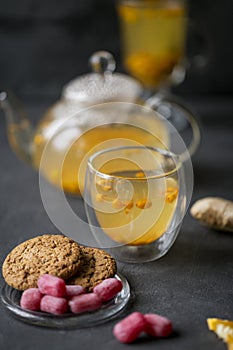 Sea buck thorn tea in glass teapot with glass cup, cookies, sweet candies near on black background