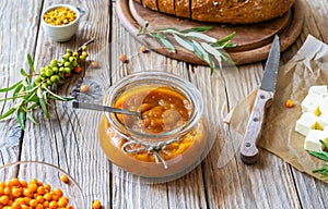 Sea buckthorn jam in a glass jar with butter, fresh berries, leaves and loaf bread