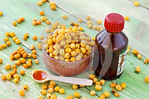 Sea-buckthorn oil and berries in a bowl on a wooden background