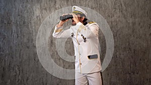 The sea captain in a white uniform looks halfway into the distance with binocular