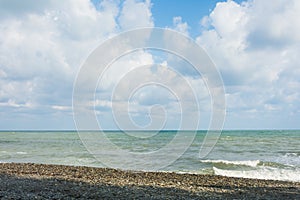 Sea coast with pebbles and blue sky with white clouds