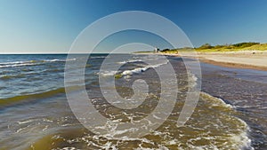 The sea coastline with beautiful rolling waves and a red lighthouse in the distance