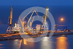 Sea commercial port at night in Mariupol, Ukraine. Industrial view. Cargo freight ship with working cranes bridge in sea port