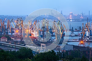 Sea commercial port at night in Mariupol, Ukraine. Industrial view. Cargo freight ship with working cranes bridge in sea port