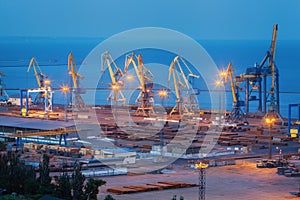 Sea commercial port at night in Mariupol, Ukraine. Industrial view. Cargo freight ship with working cranes bridge in sea port