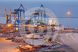 Sea commercial port at night in Mariupol, Ukraine. Industrial view. Cargo freight ship with working cranes bridge in sea port