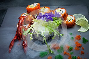 Sea crawfish and sushi on a slate dark plate with liquid smoke