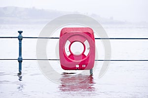 Sea flood onto street with red life safety ring during bead extreme rain and weather storm in uk