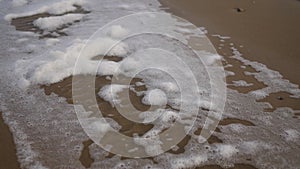 Sea foam being blown by the wind on sandy beach in slow motion. Spume flow pieces on a shore by the ocean waves on windy