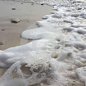 Sea foam with a wave on a sandy beach