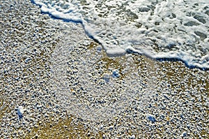 Sea foam and white pebbles of different sizes on the wet sand