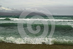 Sea foamy waves running on a pebble beach on a cloudy day