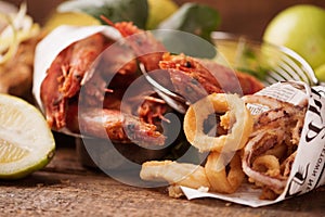 Sea food served on news paper: squid rings, grilled prawns, octopus, lemons on rustic wooden table